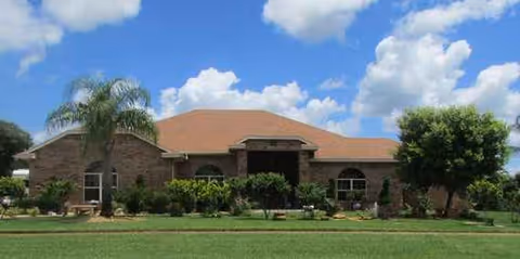 Single-story brick facility with an arched entry, manicured shrubs, and palm trees at the front.