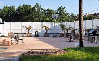 Outdoor courtyard at TBI Residential Services Inc with tables, chairs, potted plants, and a basketball hoop.