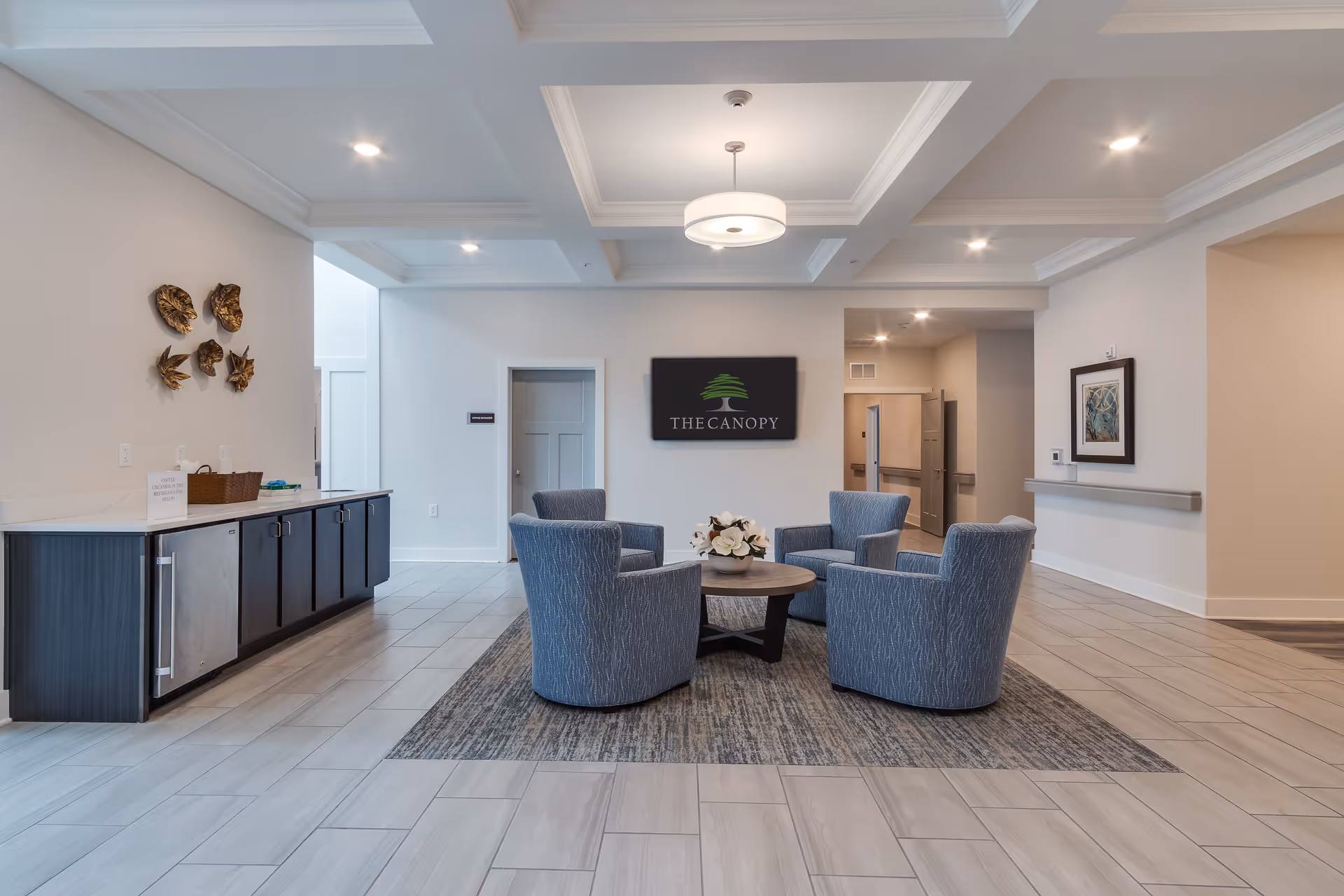 A modern lobby seating area with four blue armchairs around a coffee table under coffered ceilings and a sign reading 'The Canopy' on the back wall.