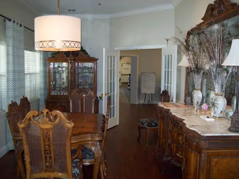 Antique-style dining room with a wooden table and chairs, china cabinet, sideboard, and French doors opening to a hallway.