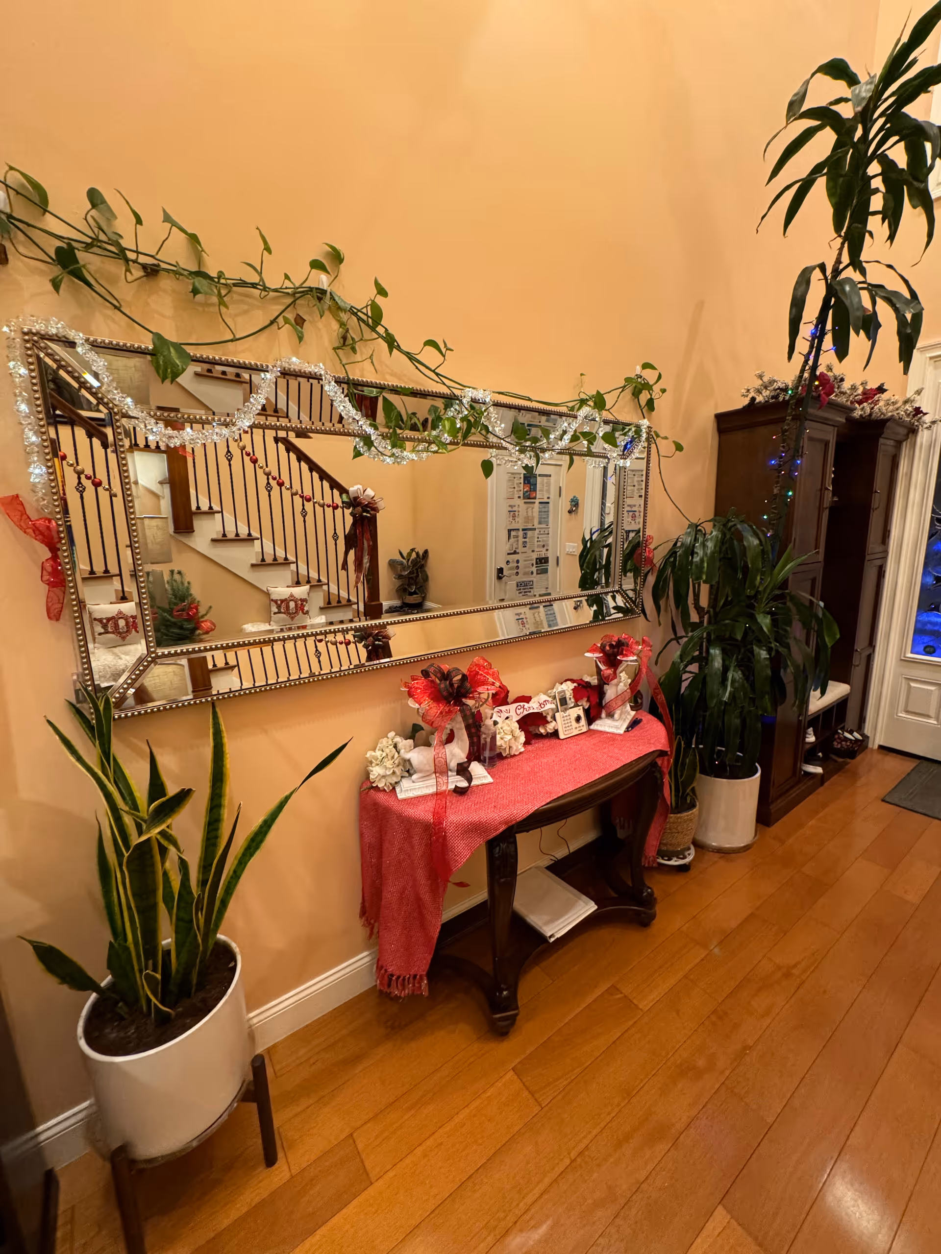 Entry hallway with a large wall mirror above a decorated console table, potted plants, and a staircase reflected in the mirror.