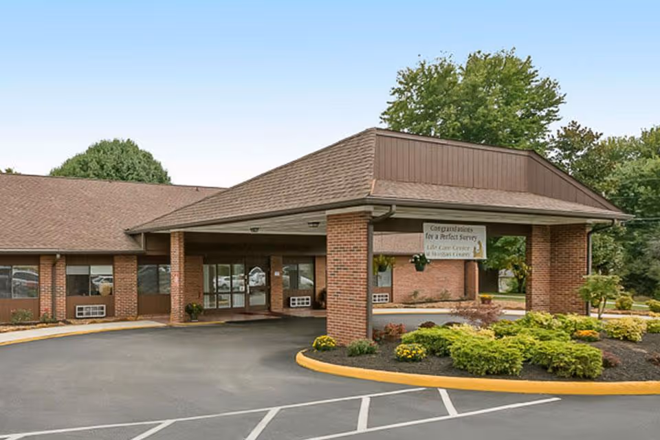 Front entrance of a one-story brick senior living facility with a covered drive-through portico and landscaped beds.
