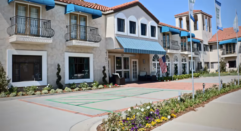 Exterior view of Sunnycrest Senior Living with balconies, awnings, and a landscaped entrance.