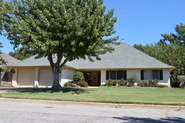 Single-story senior living facility with front lawn, large tree, and shrubs.