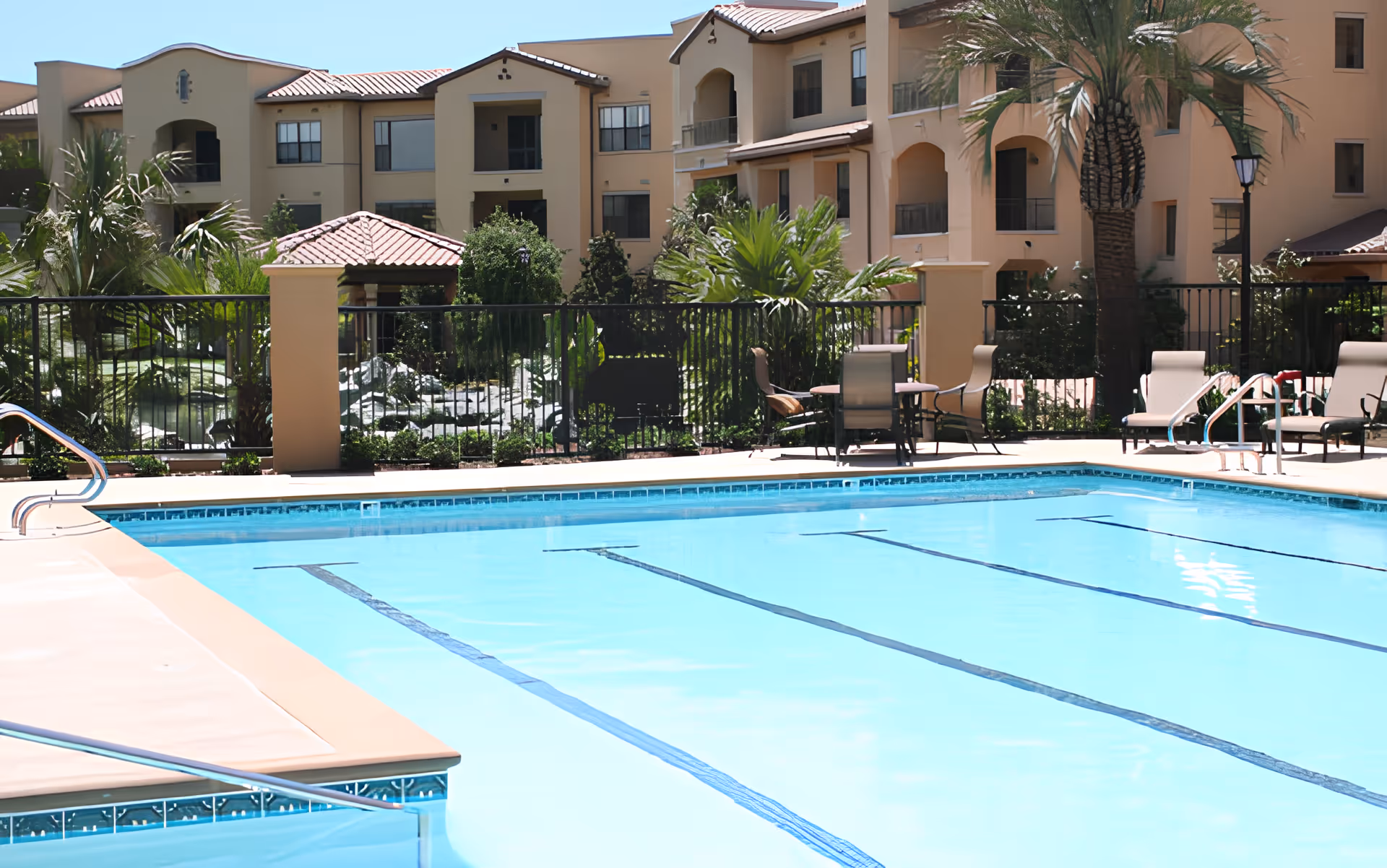 Outdoor swimming pool with lounge chairs and patio furniture in front of a multi-story residential building.