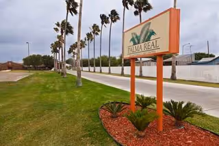 Palma Real facility sign beside a grassy median with palm trees