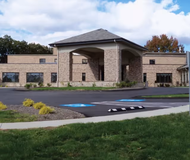 Exterior view of the Vincentian Home building showing a brick facade with a covered entrance, parking spaces including handicapped spots, landscaped areas with grass and small shrubs, and a partly cloudy sky.