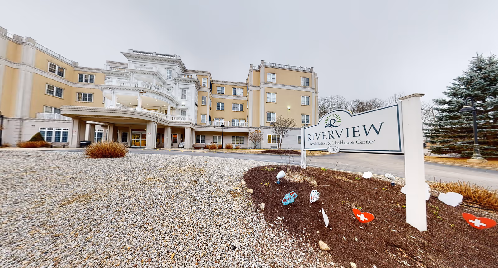 Front exterior of Riverview Rehabilitation & Healthcare Center with the facility sign in the foreground and the multi-story building and driveway behind it.