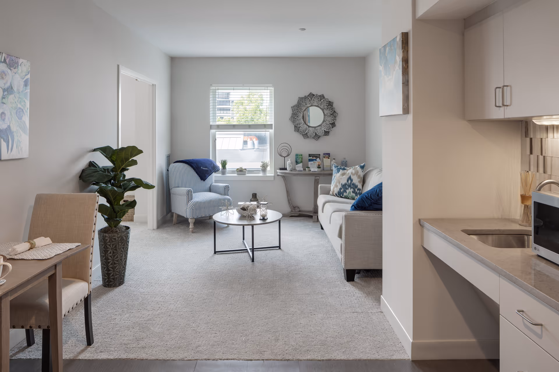 Open-plan living room and kitchenette with a sofa, armchair, coffee table, and neutral decor.