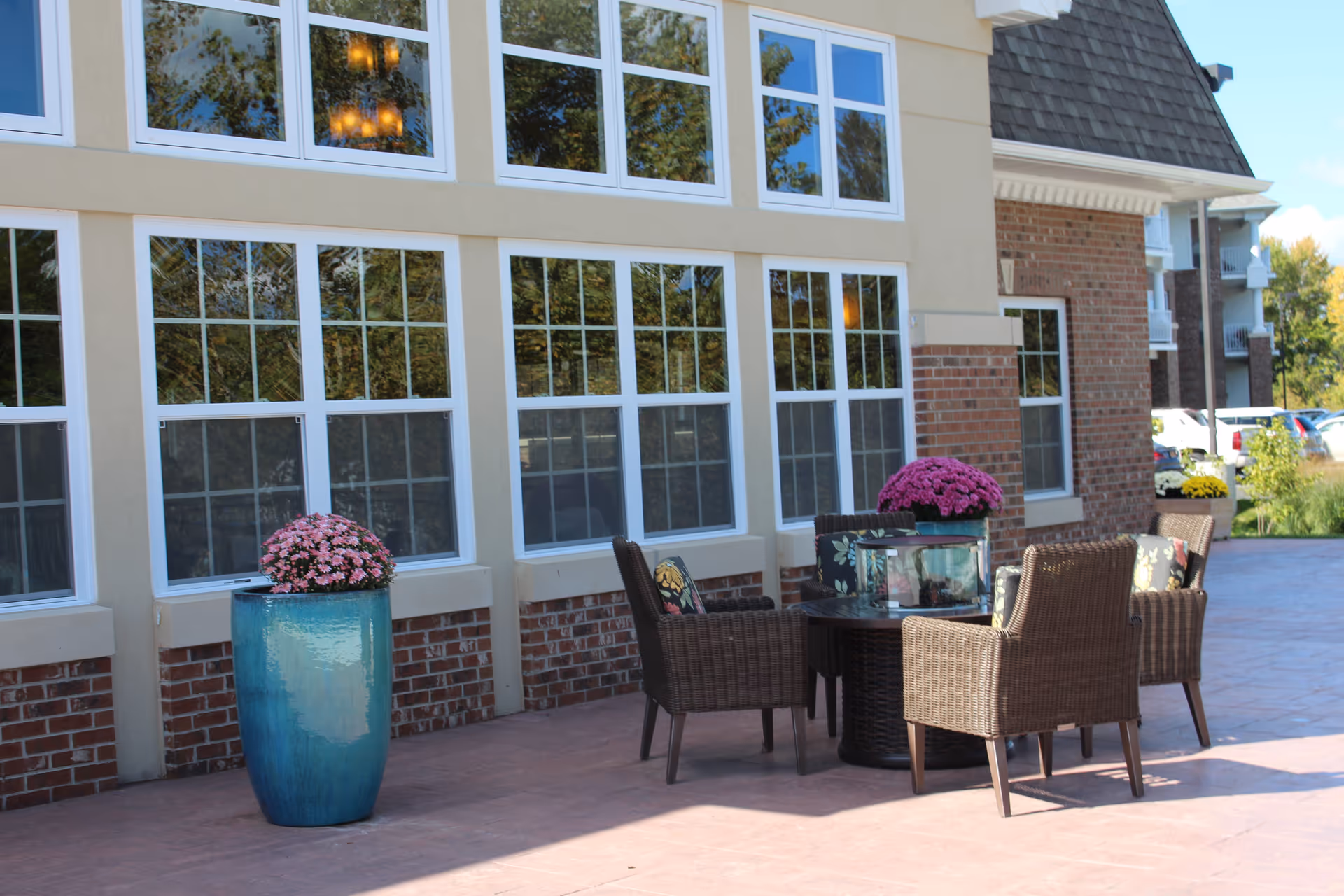 Outdoor patio with wicker chairs, a table and potted flowers in front of a retirement community building.