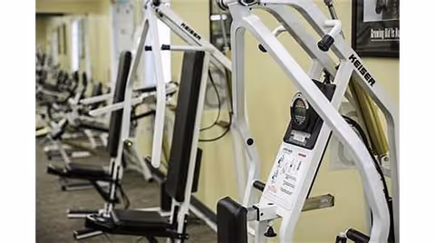 Row of white exercise machines and weight equipment arranged in a fitness room.