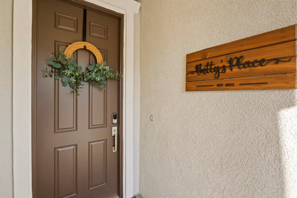 The entrance door of Betty's Place Assisted Living with a decorative wreath and a wooden sign.