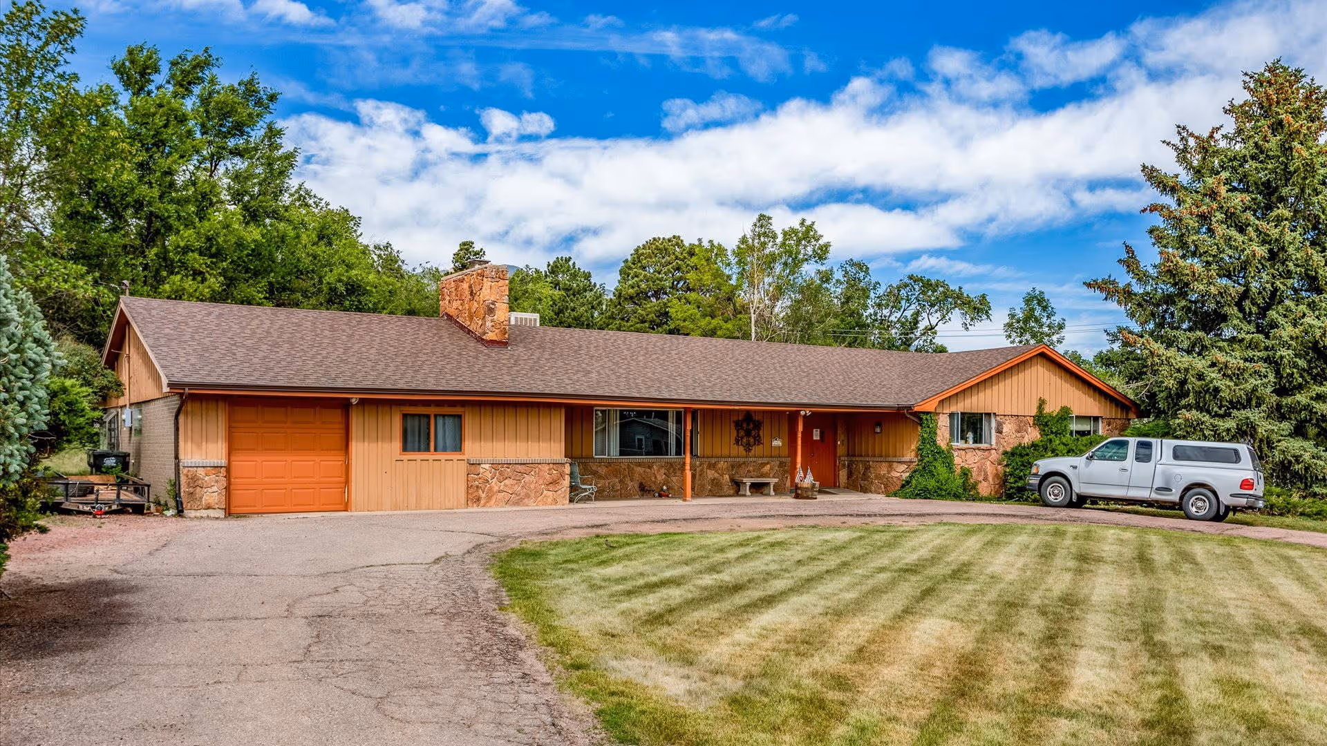 Ranch-style single-story assisted living building with an attached garage, circular driveway, manicured lawn, and a white pickup truck parked at the entrance.