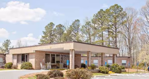A single-story brick senior living center with a covered entrance and surrounding parking.