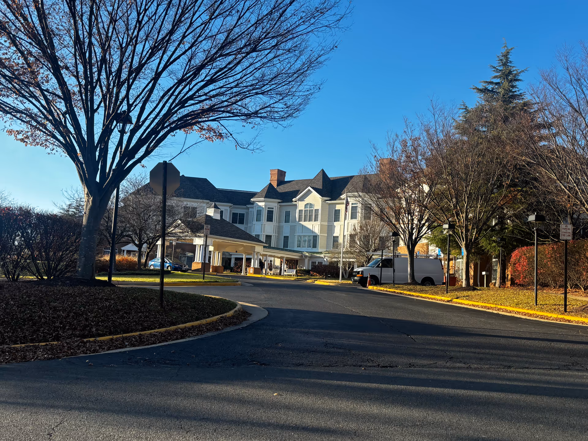 Front view of a multi-story white senior living building with a covered entrance, circular driveway, and trees.