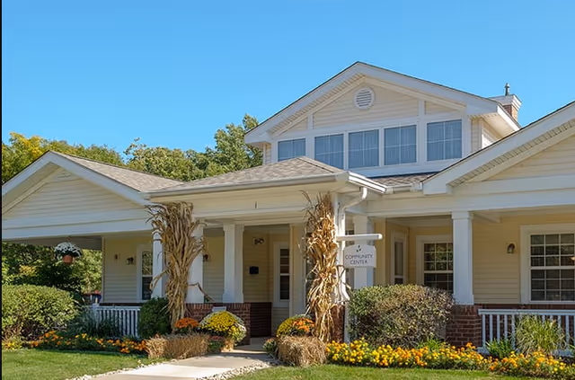 Cream-colored single-story community center building with a covered porch, white columns, landscaping, and a small 'Community Center' sign.