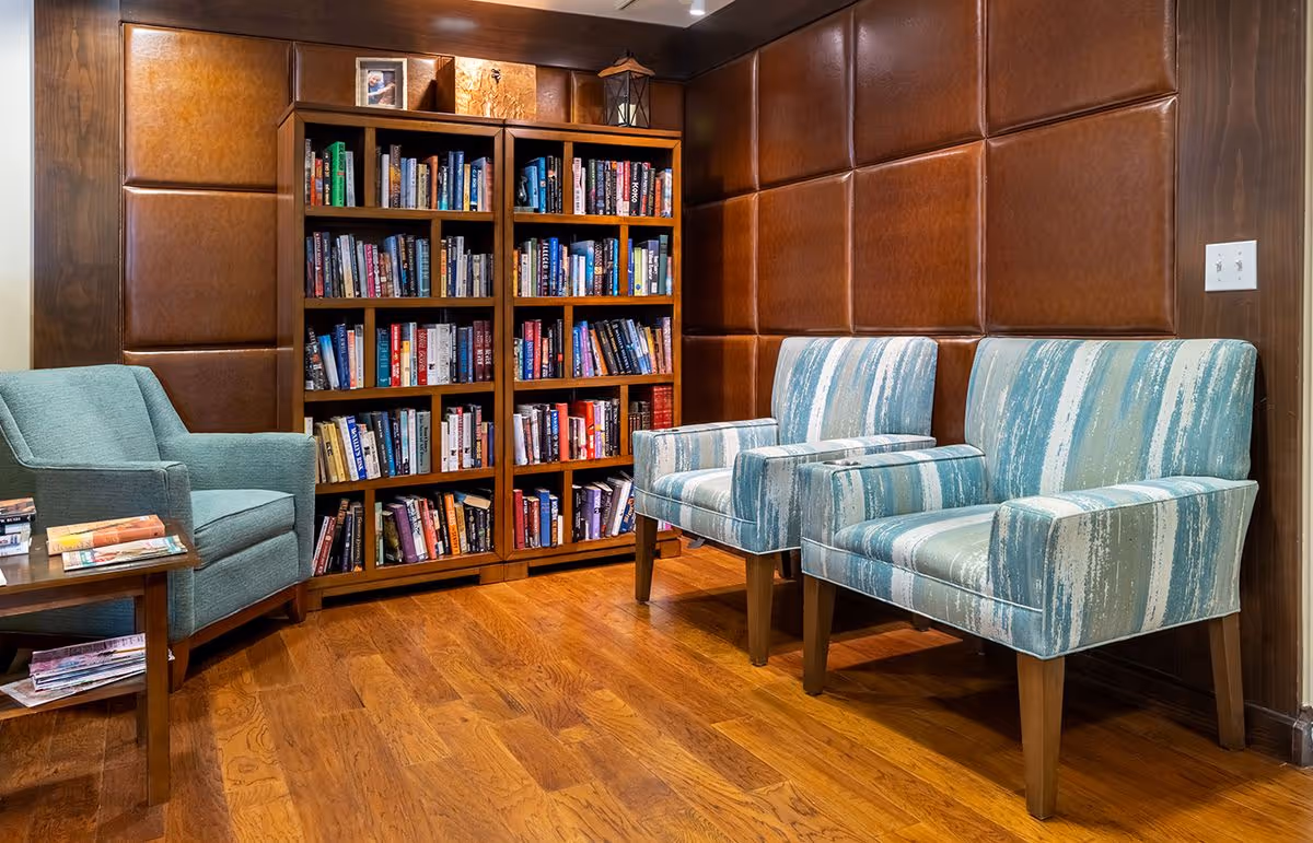 Cozy reading corner with a bookshelf and two striped armchairs plus a teal chair against a leather-paneled wall.