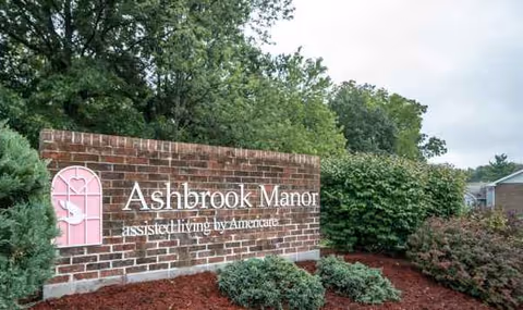 Ashbrook Manor brick sign with landscaping and trees in front.