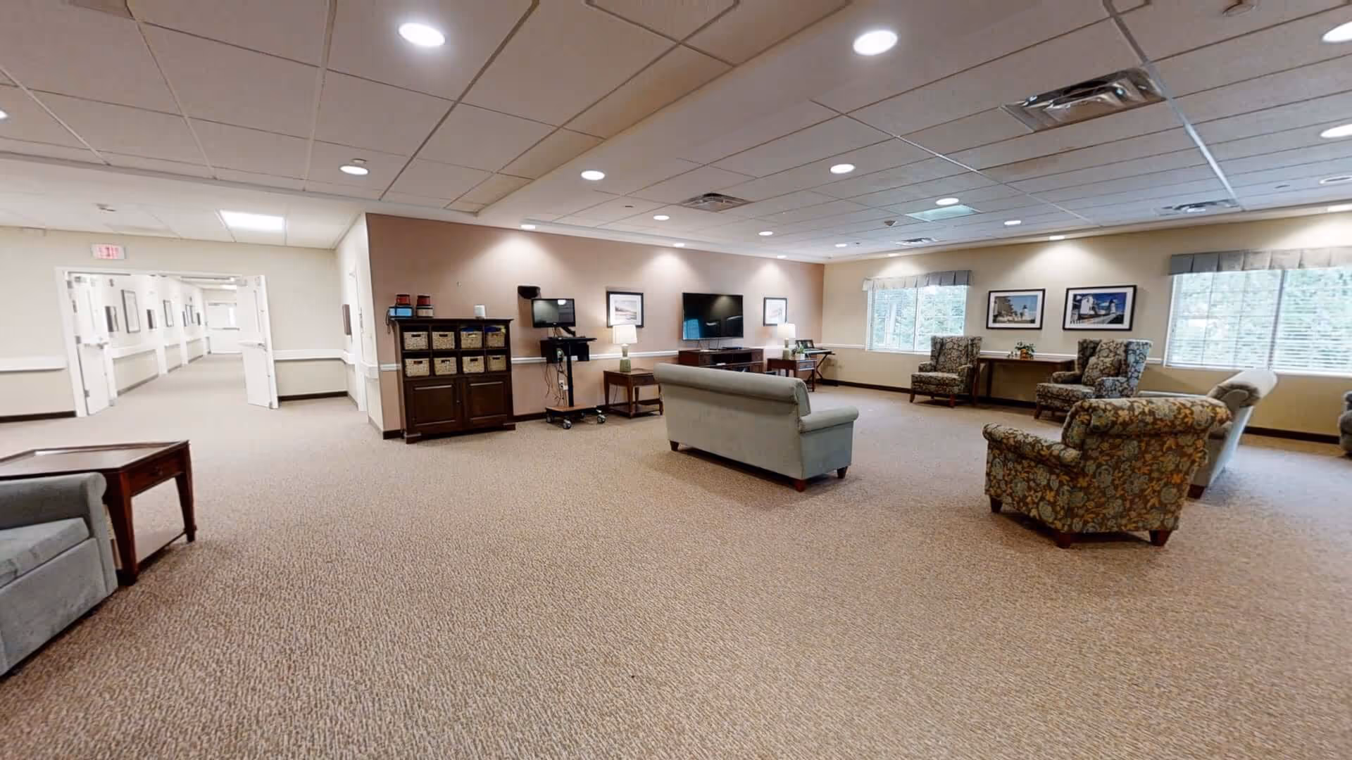 Spacious senior living common lounge with sofas, armchairs, a TV, and large windows.