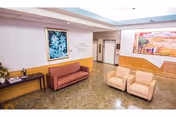 A nursing facility lobby with seating, artwork on the walls, and an elevator bank.