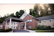 Front exterior of a multi-story brick and siding senior living building with a covered entryway and driveway framed by trees.
