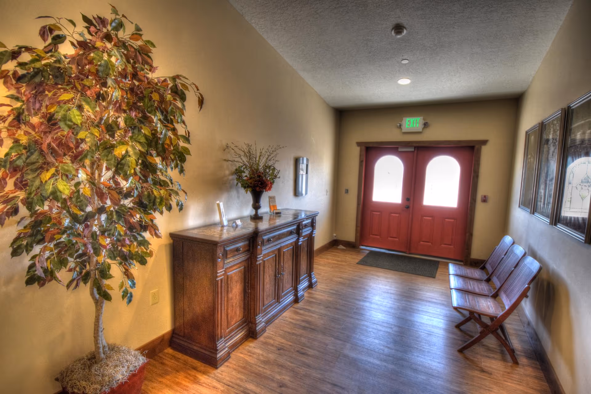 Entrance hallway with double red doors, a wooden sideboard, potted plant and bench seating along the wall.