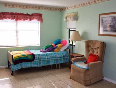 Pastel-colored bedroom with a single bed, stuffed animals, and a brown recliner.