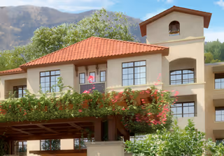 Mediterranean-style multi-story retirement building with red tile roof, balconies and flowering vines.