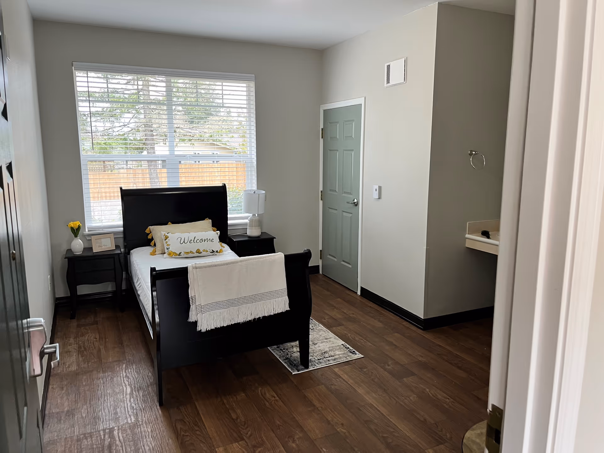 Bright single-occupancy bedroom with a sleigh bed, bedside tables, large window and a small sink area.