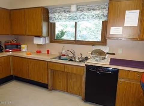Wooden cabinet-lined kitchen with sink, window, dishwasher, and small appliances.