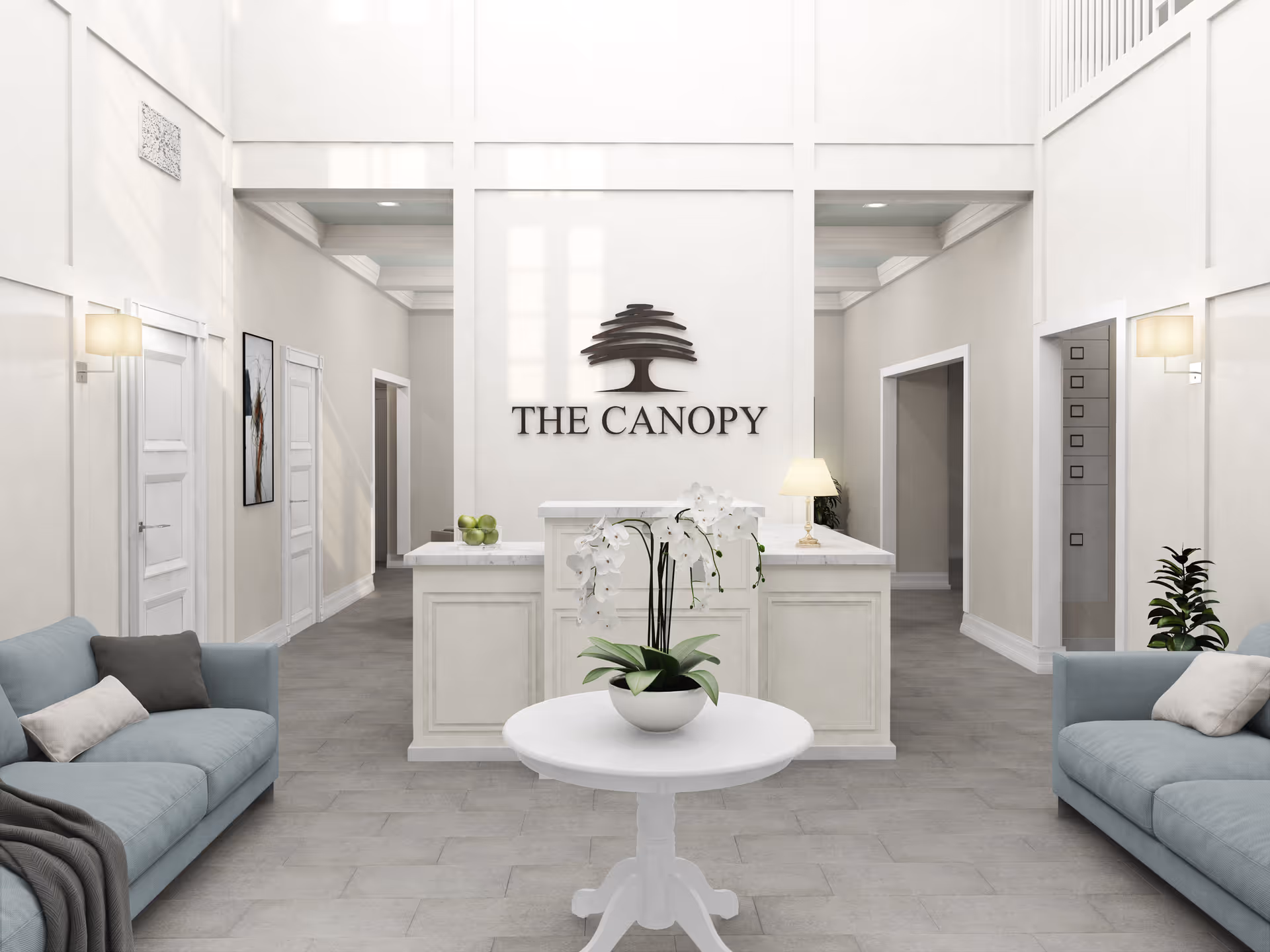Bright, airy reception lobby with a central round table holding an orchid, two sofas, and a front desk beneath a 'The Canopy' wall logo.