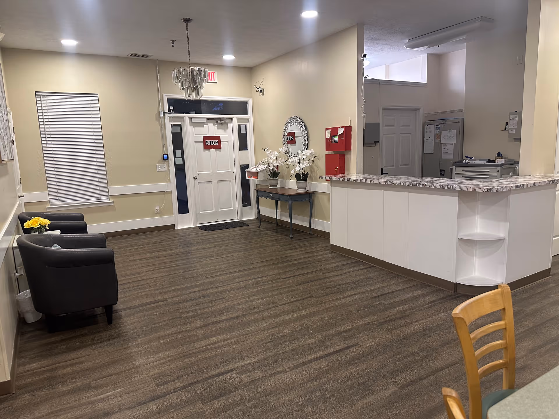 Reception/lobby area with a front door marked STOP, seating, a small console table with flowers, and a reception desk.