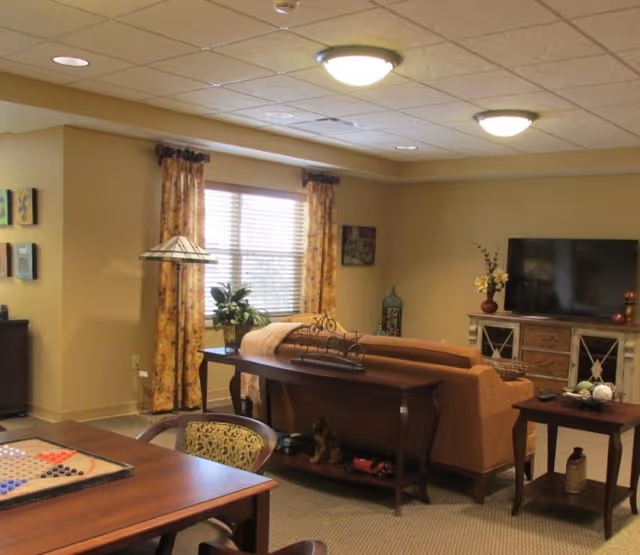 Communal living room with a sofa, TV on a console, a game table in the foreground, and decorative curtains and lighting.