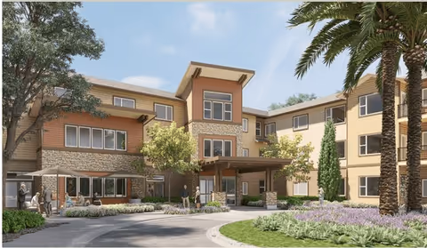 Three-story senior living building with a covered main entrance, landscaped circular driveway and palm trees.