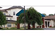 Exterior view of a two-story senior living facility with entrance, trees, and parking.