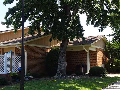 Single-story brick building front with a large tree, small lawn, and a covered entry.