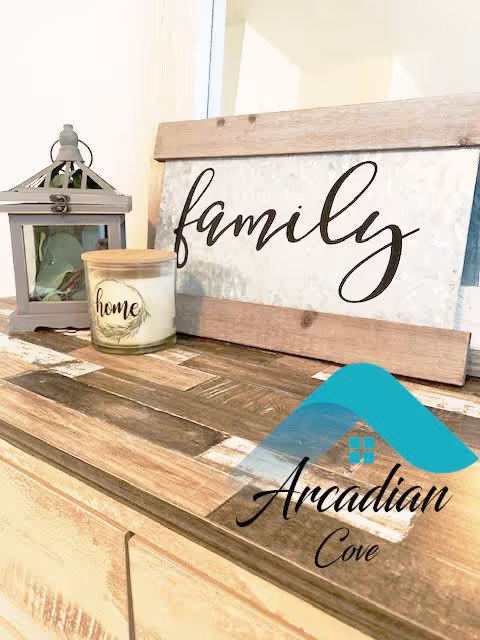 A decorative wooden sign with the word 'family' written in cursive, placed on a wooden surface next to a candle labeled 'home' and a small lantern with greenery inside.
