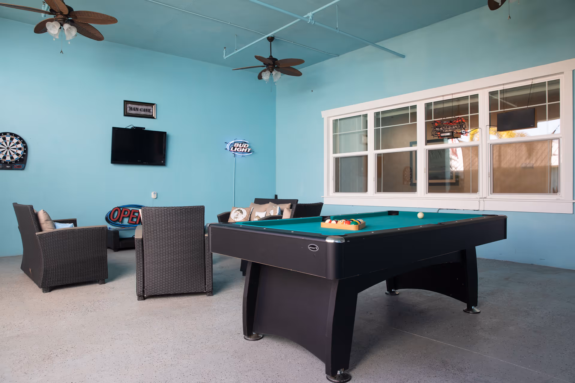 Indoor recreation room with a pool table, seating area, wall-mounted TV and game decor on turquoise walls.