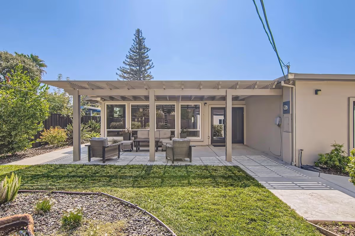 Backyard patio with a pergola, outdoor seating, and a lawn in front.