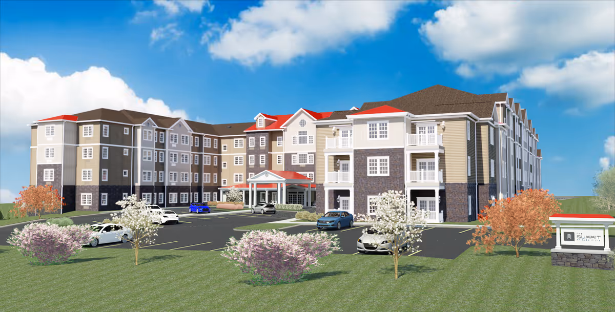 Exterior view of a large multi-story senior living facility building with beige and brown siding, white trim, and red roofs. The building has multiple windows and balconies. There is a parking lot with several cars in front, landscaped with green grass, flowering bushes, and small trees. A sign near the entrance reads 'The Summit at Glen Mills.' The sky is blue with some clouds.