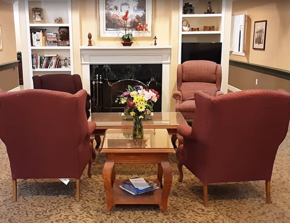 Cozy seating area with four upholstered armchairs arranged around a coffee table and a vase of flowers in front of a fireplace and built-in shelves.