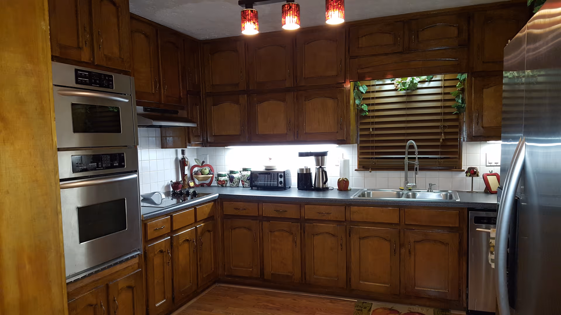 Wood-paneled kitchen with stainless steel appliances, double sink, dark countertops, and wooden cabinets.