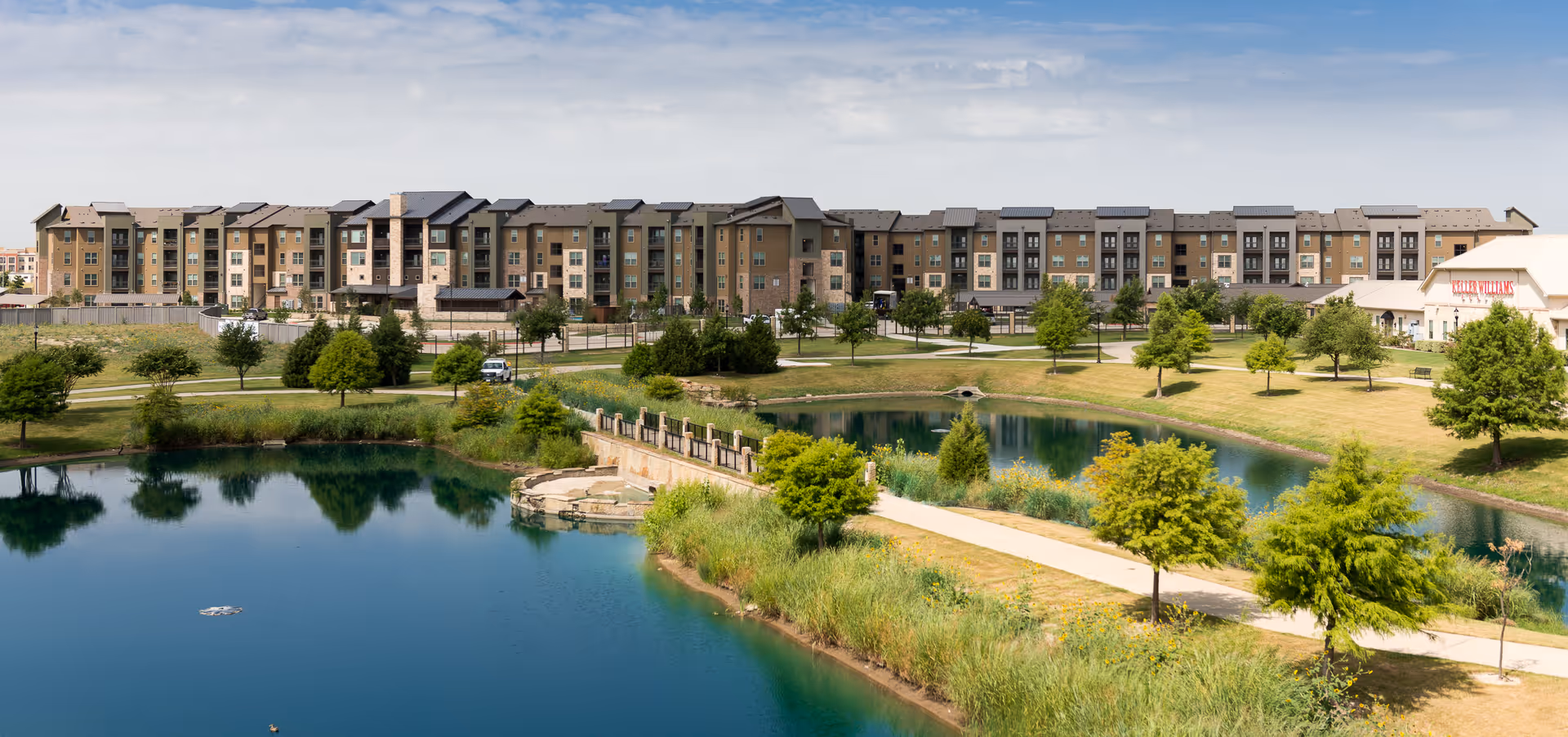Larkspur at Twin Creeks senior living campus along a pond with green grounds.