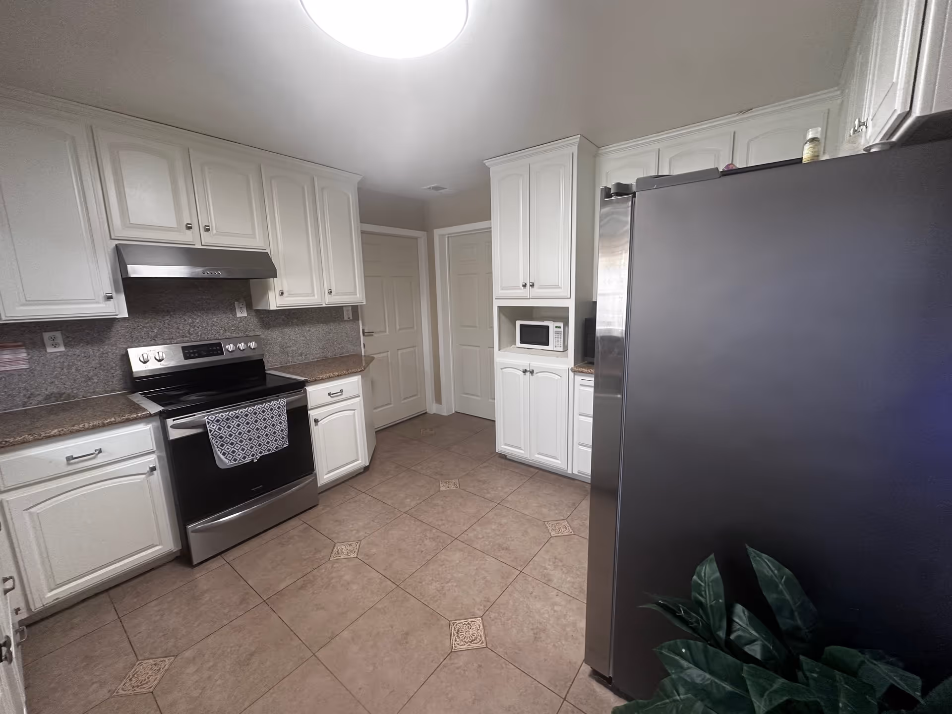 Bright white kitchen with stainless stove, fridge, and microwave in a senior living facility.