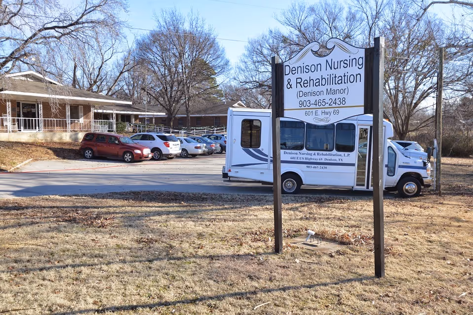 Front view of Denison Nursing & Rehabilitation sign and building with parked cars and a shuttle bus.