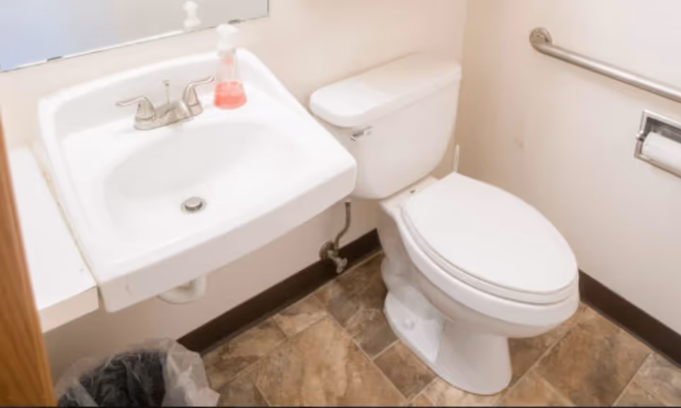 Small accessible bathroom with a sink, soap dispenser, toilet, grab bar, and tiled floor.