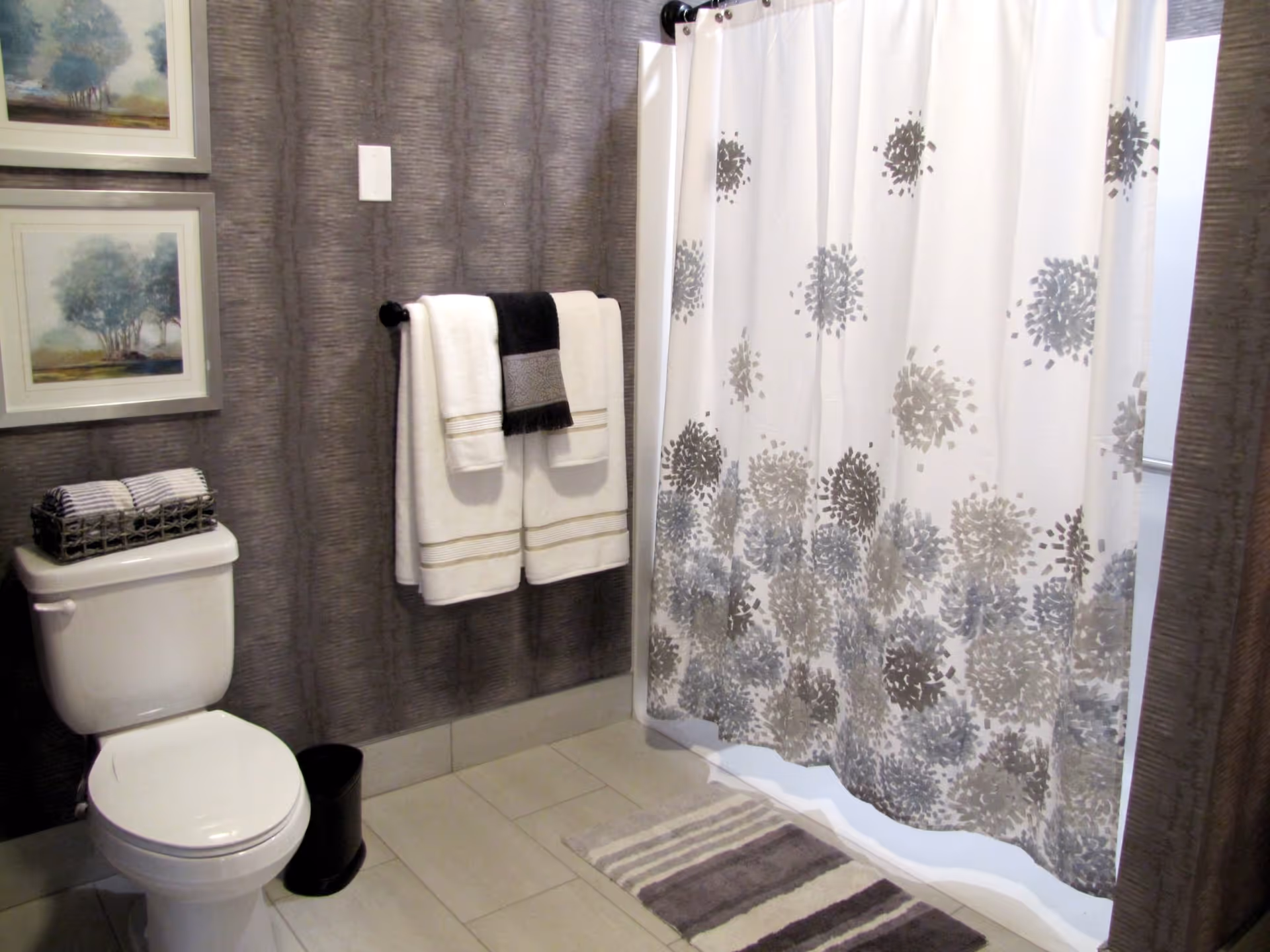 A bathroom with a toilet, towel rack holding folded towels, and a floral-patterned shower curtain.