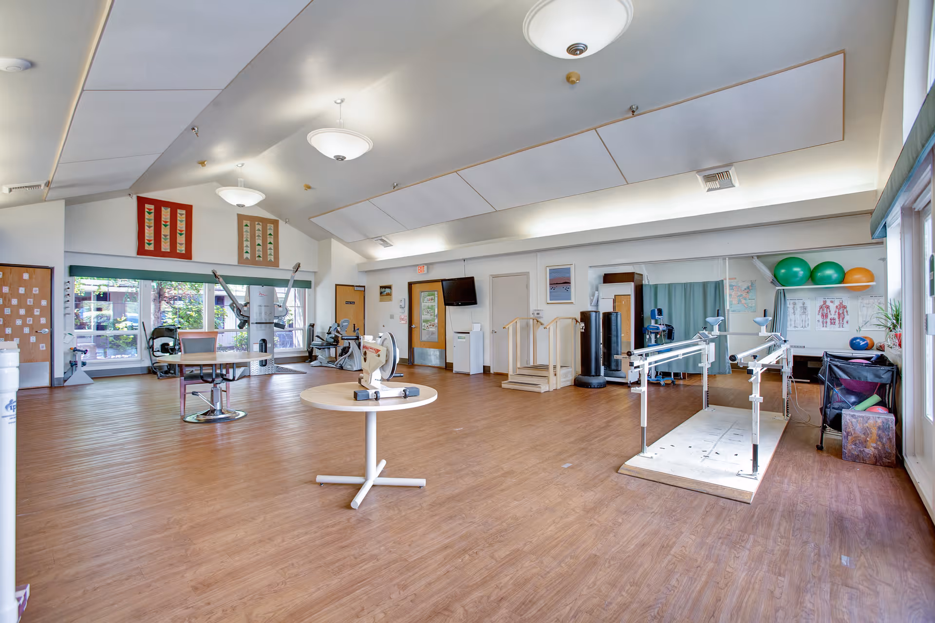 Spacious rehabilitation/exercise room with parallel bars, therapy equipment, exercise balls and seating.