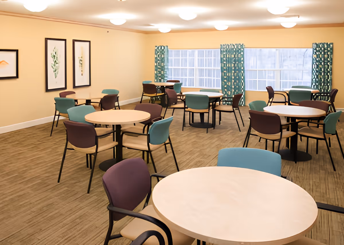 Bright communal dining/activity room with round tables and colorful chairs.