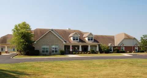 Single-story building with a combination of brick and siding exterior, featuring a covered entrance with two dormer windows on the roof, surrounded by a well-maintained lawn and a paved driveway under a clear sky.